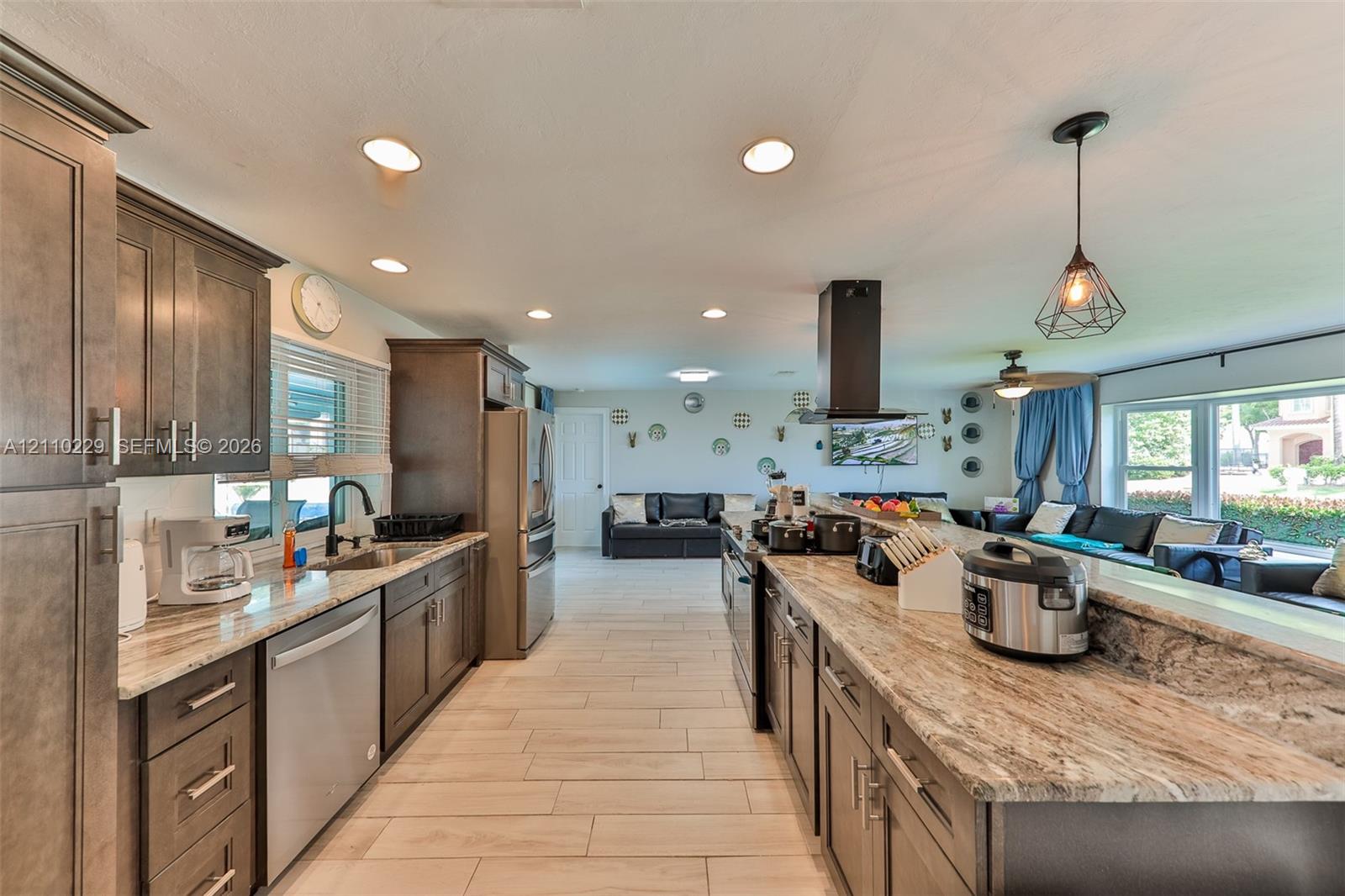 Kitchen featuring dark wood cabinetry, expansive natural stone countertops, tile flooring, stainless steel appliances, and a modern geometric pendant light