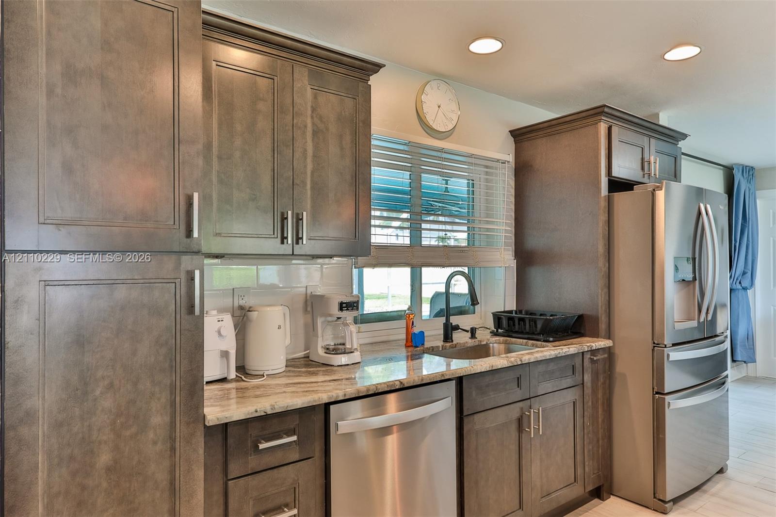 Kitchen featuring dark wood-finish cabinetry, stone-patterned countertops, white tile backsplash, stainless steel appliances, and a matte black gooseneck faucet