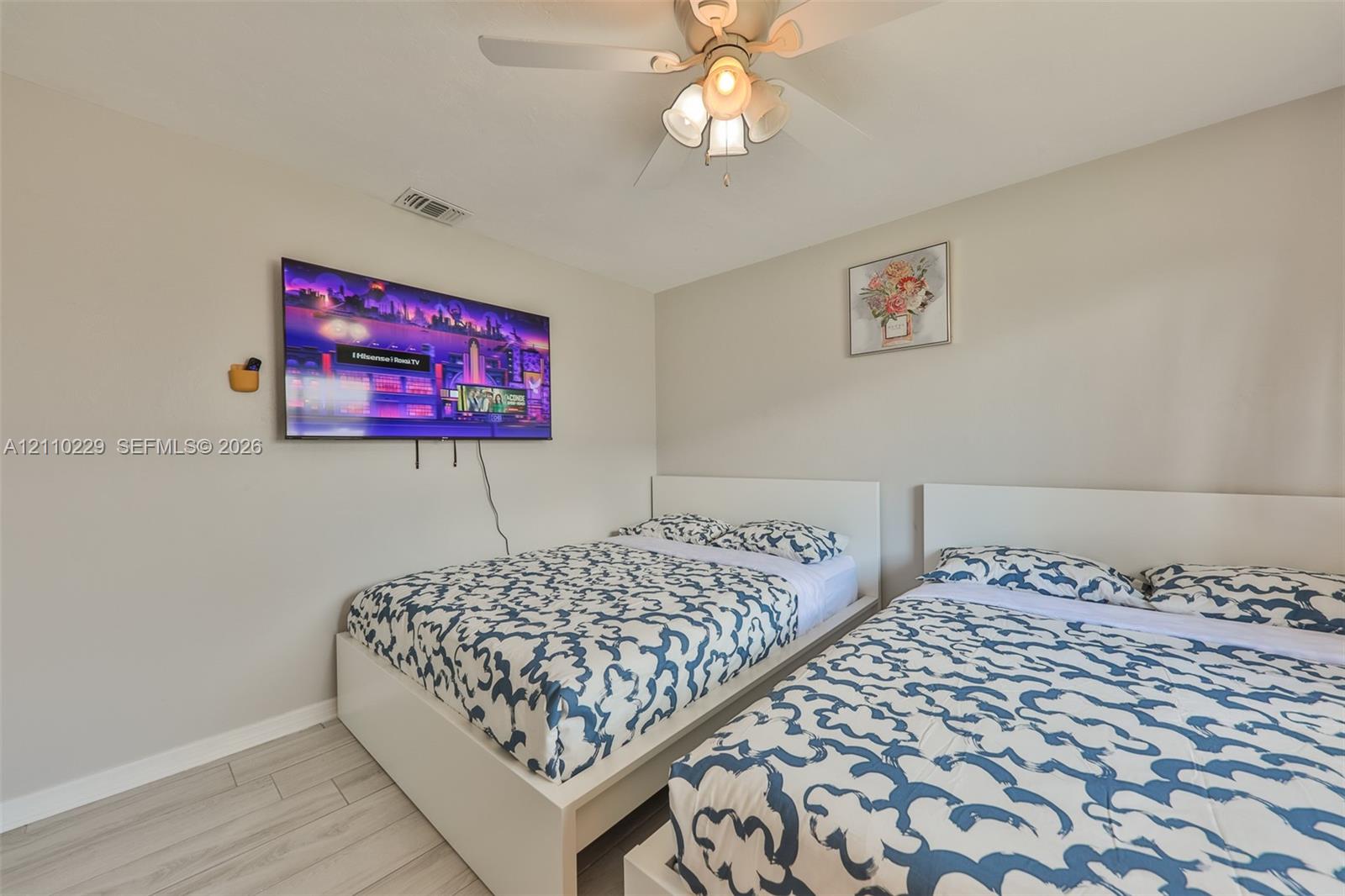 Neutral-toned interior featuring wood-finish flooring, a ceiling fan with integrated lighting, and a wall-mounted display