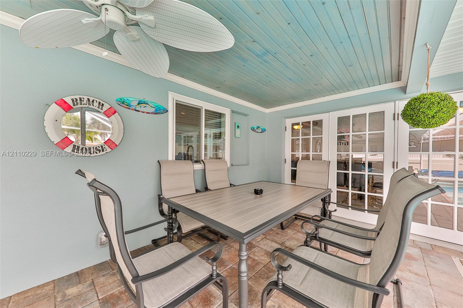 Covered patio featuring a blue-stained wood tongue-and-groove ceiling, stone-paver flooring, a white ceiling fan, and double-paned glass French doors