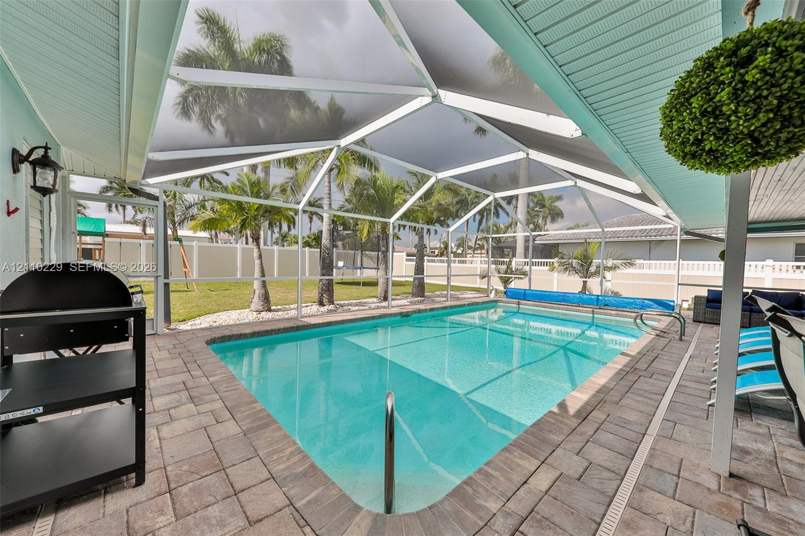 Screen-enclosed pool area featuring concrete paver decking, vaulted tongue-and-groove ceiling, and a fenced backyard with palm trees