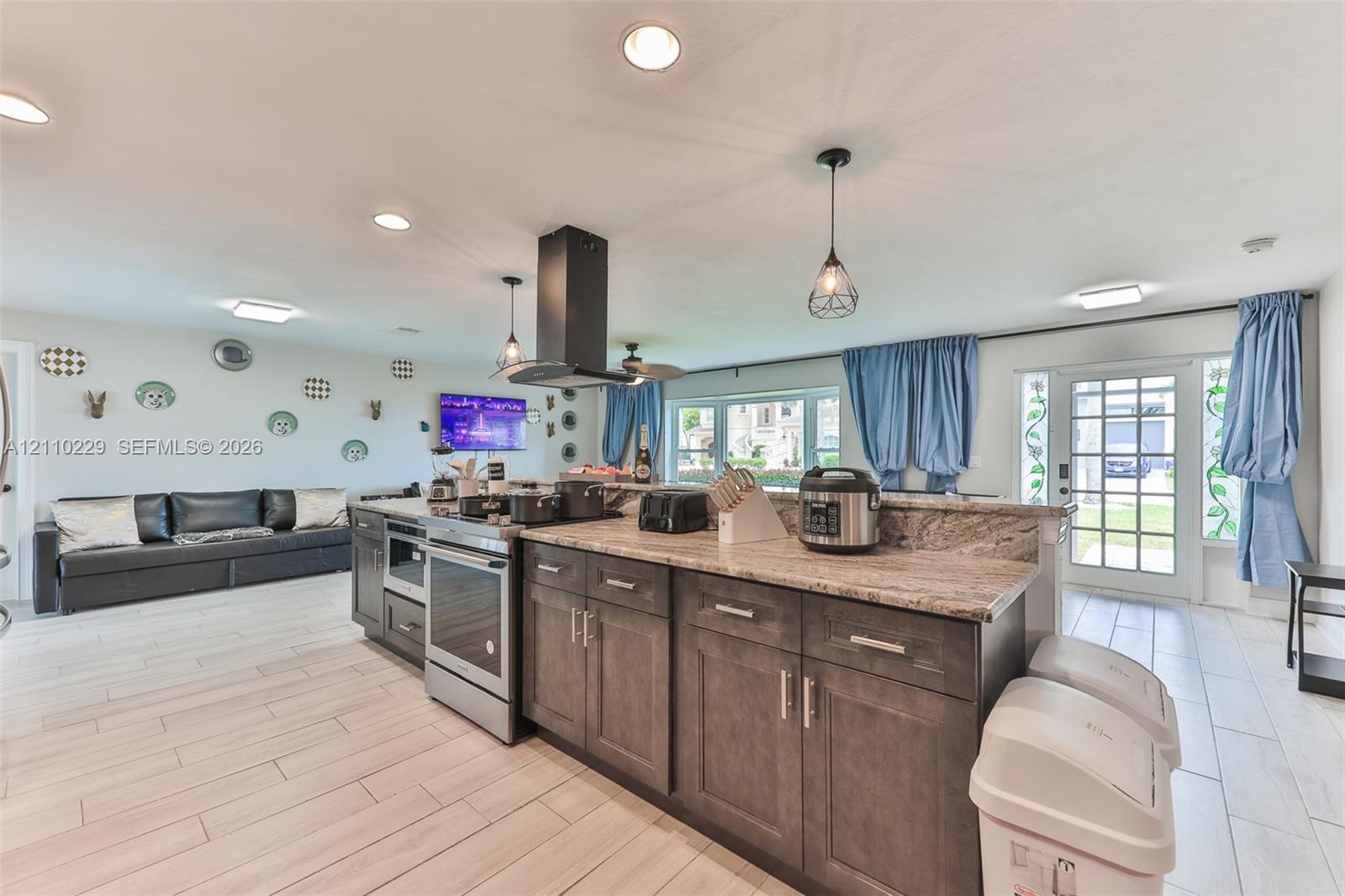 Kitchen featuring a central island with stone-finish countertops, stainless steel appliances, dark wood cabinetry, a suspended range hood, and tile flooring