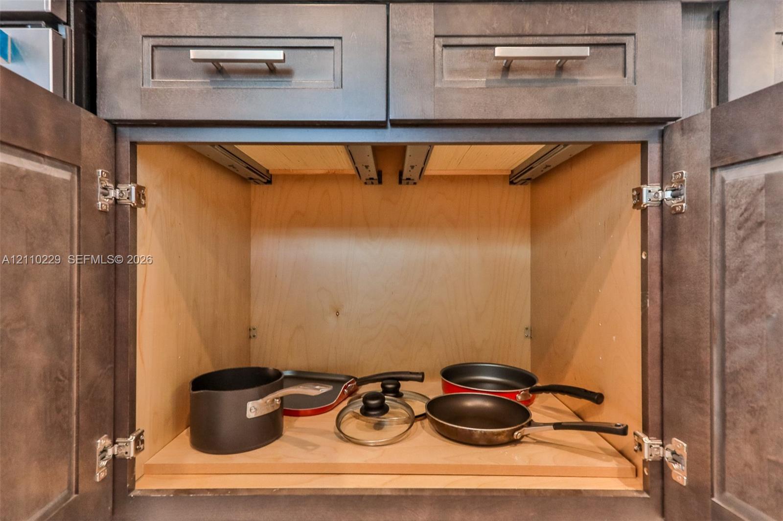 Dark-toned cabinetry featuring shaker-style doors, horizontal brushed metal hardware, and an interior slide-out wooden shelf