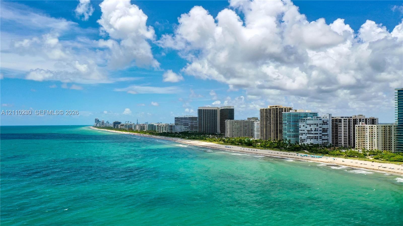 Coastal aerial perspective featuring turquoise ocean waters, a sandy shoreline, and a shoreline of high-rise structures
