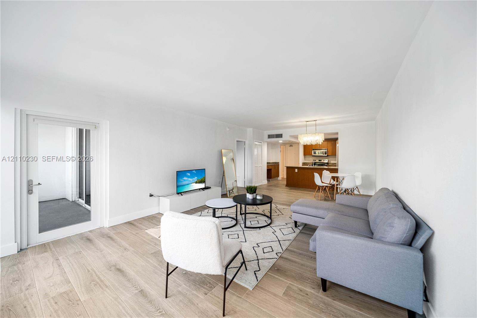 Open-concept interior featuring light wood-finish flooring, glass-paned door, recessed ceiling lighting, and kitchen with wooden cabinetry