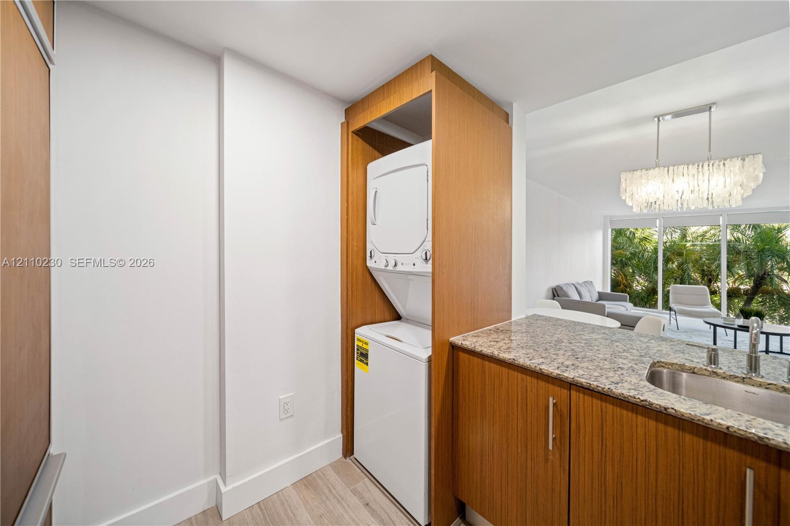 Built-in stacked laundry unit within custom wood-veneer cabinetry, stone countertop, stainless steel undermount sink, and wood-finish flooring