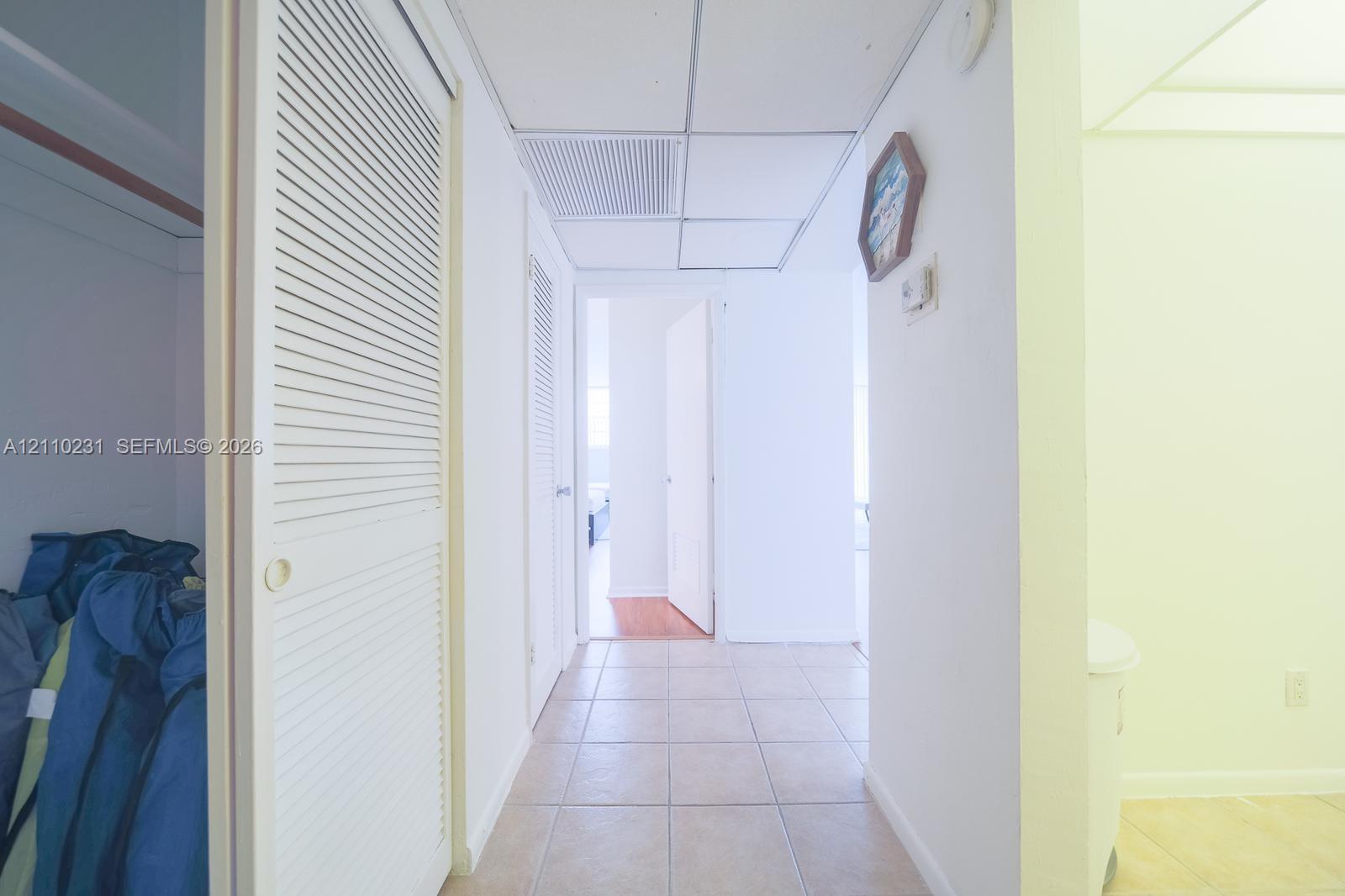 Hallway featuring ceramic tile flooring, bi-fold louvered closet doors, and a suspended drop ceiling