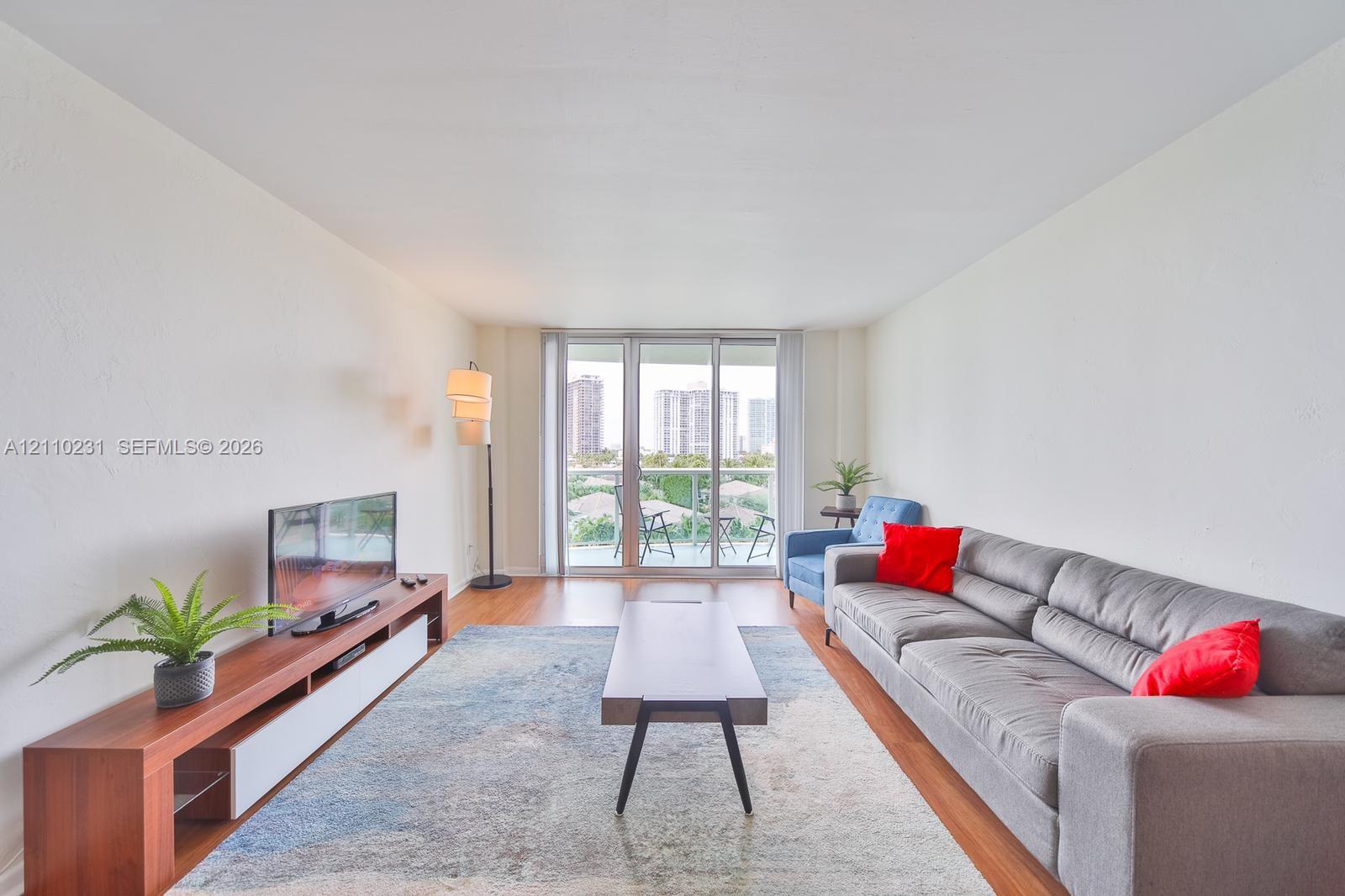 Living area featuring wood-finish flooring, white walls, and floor-to-ceiling glass sliding doors opening to a private balcony