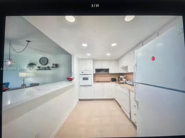 Kitchen featuring white cabinetry, solid-surface countertops, built-in wall oven, recessed ceiling lighting, and a peninsula with counter seating