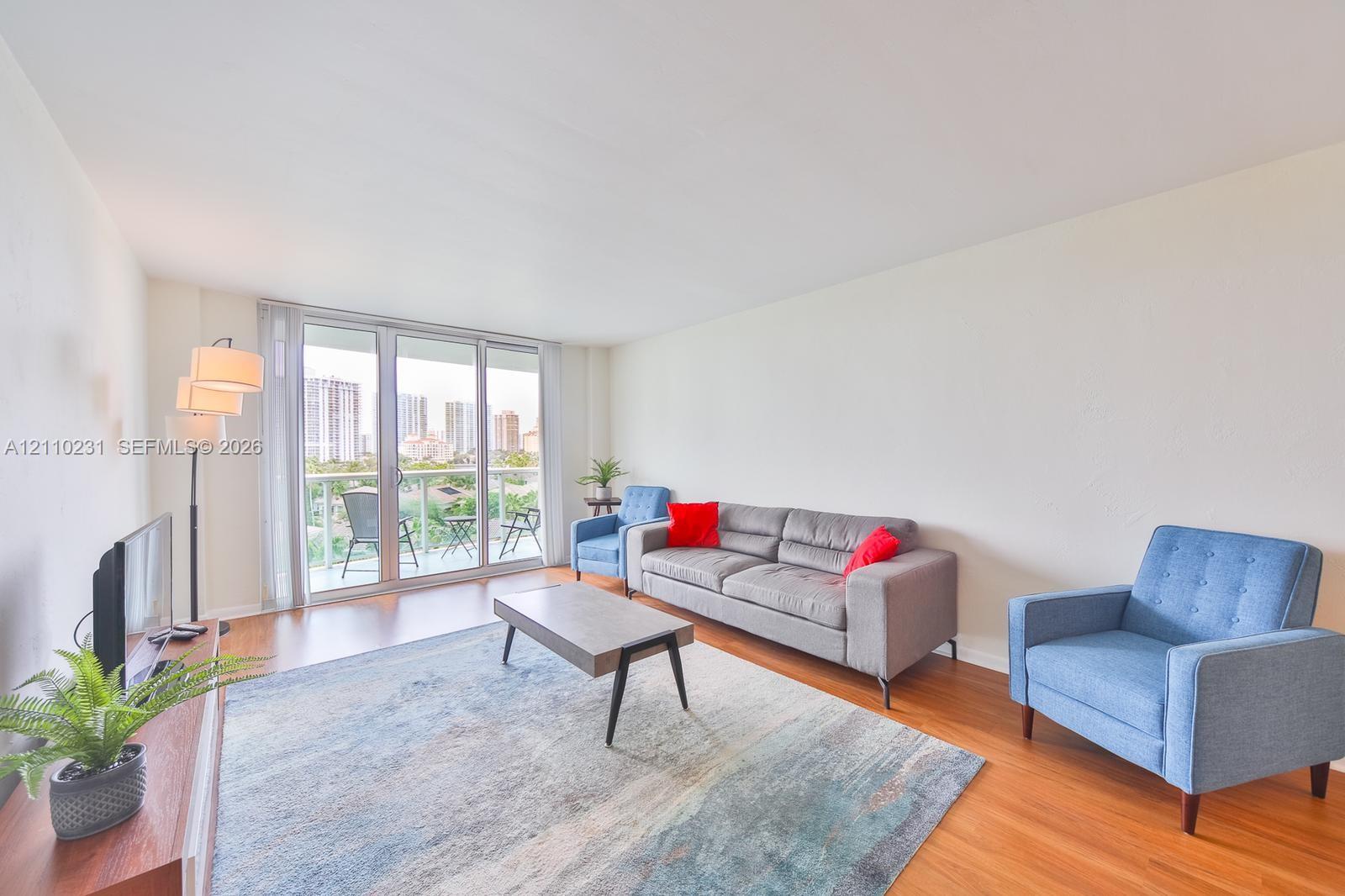 Living area featuring wood-finish flooring and expansive floor-to-ceiling glass doors opening to a balcony