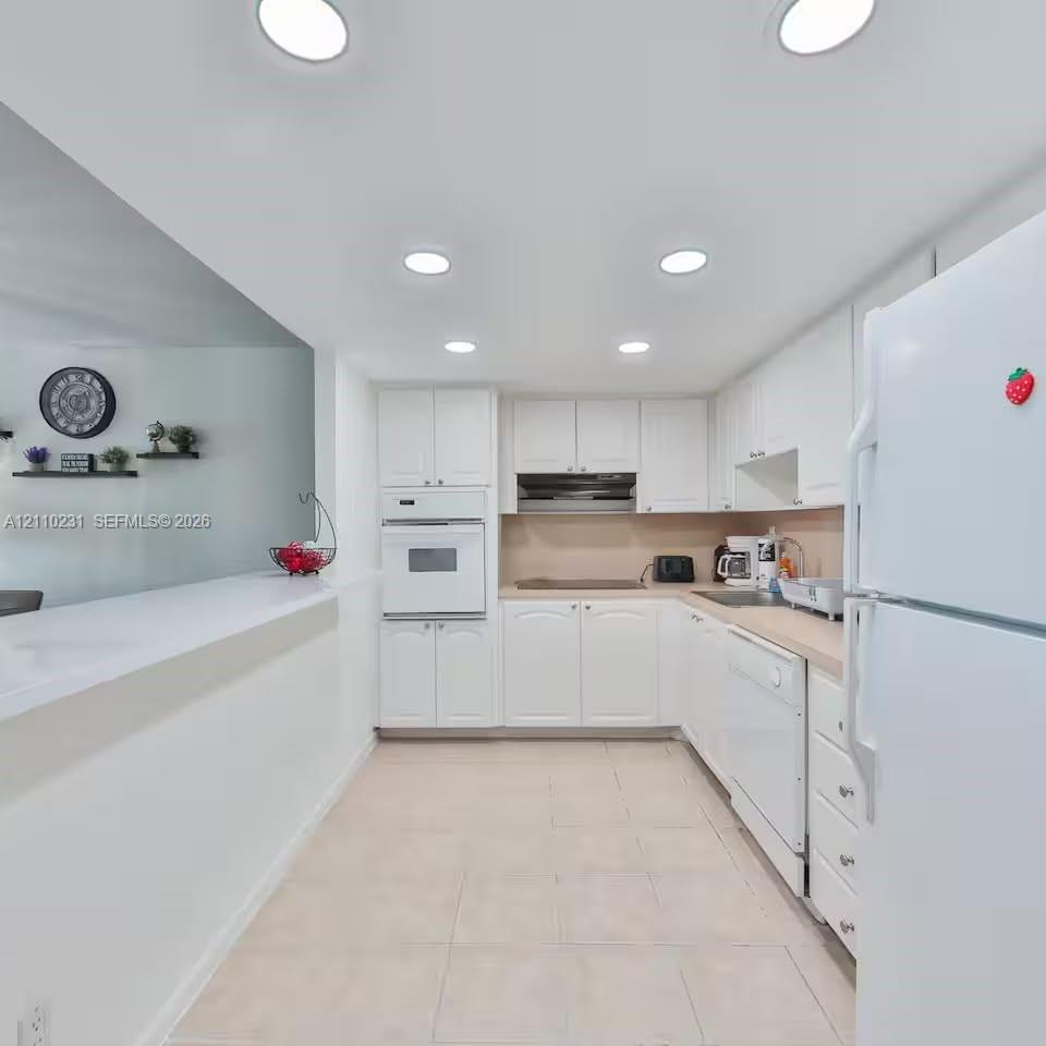 Kitchen featuring white cabinetry, recessed lighting, tile flooring, integrated wall oven, and a peninsula counter Kitchen featuring white cabinetry, recessed lighting, tile flooring, integrated wall oven, and a peninsula counter