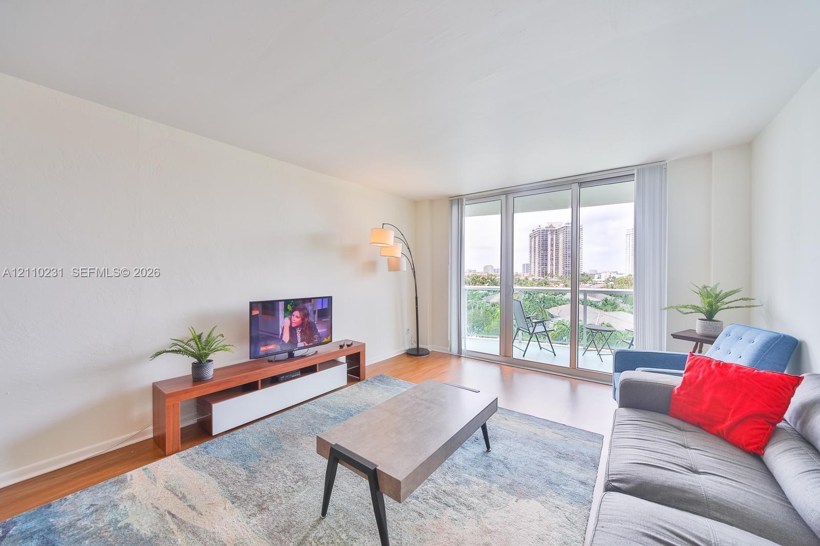 Living area featuring wood-finish flooring, floor-to-ceiling glass sliding doors, and a private balcony