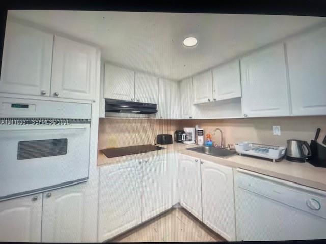 Kitchen featuring white shaker-style cabinetry, solid-surface countertops, built-in wall oven, flat cooktop, and undermount stainless steel sink Kitchen featuring white shaker-style cabinetry, solid-surface countertops, built-in wall oven, flat cooktop, and undermount stainless steel sink