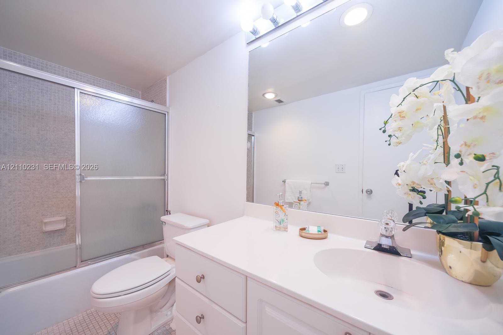 Bathroom featuring white vanity cabinetry, integrated countertop with a molded sink, polished chrome faucet, full-width mirror, and a shower-tub combination with a sliding glass door