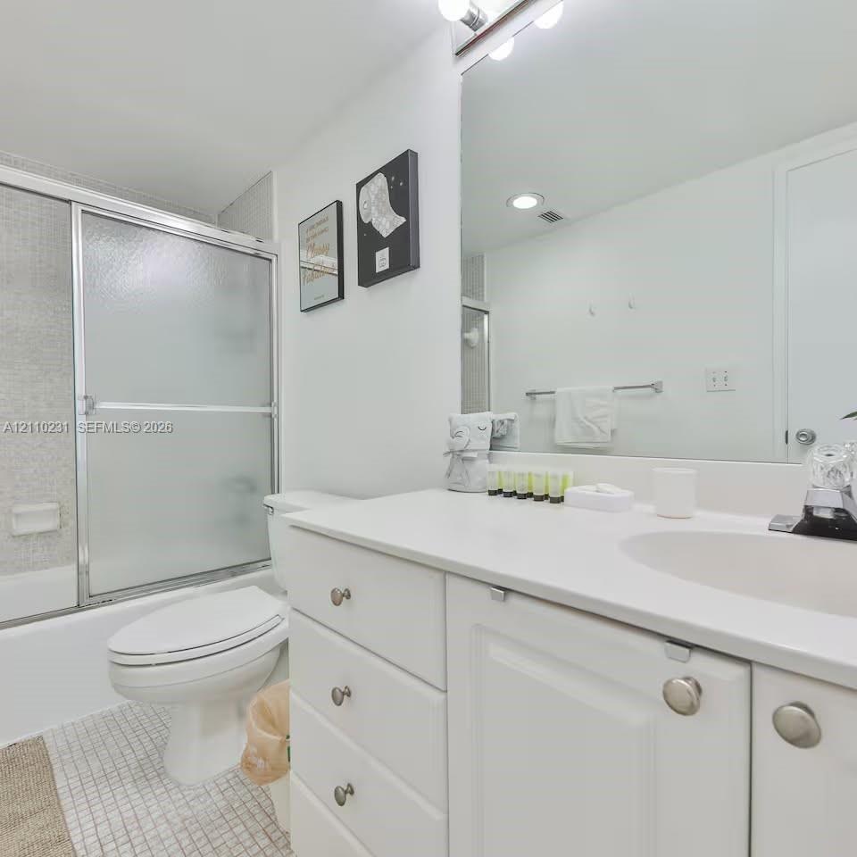Bathroom featuring a white vanity with integrated basin, polished metal hardware, a wall-spanning mirror, frosted glass sliding shower enclosure, and mosaic floor tile Bathroom featuring a white vanity with integrated basin, polished metal hardware, a wall-spanning mirror, frosted glass sliding shower enclosure, and mosaic floor tile