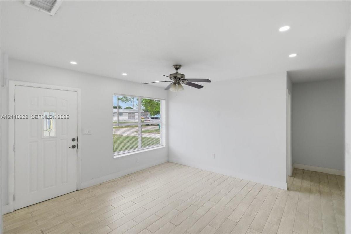 Interior space featuring wood-finish tile flooring, recessed ceiling lighting, a multi-blade ceiling fan, and a six-panel entry door with an integrated glass light