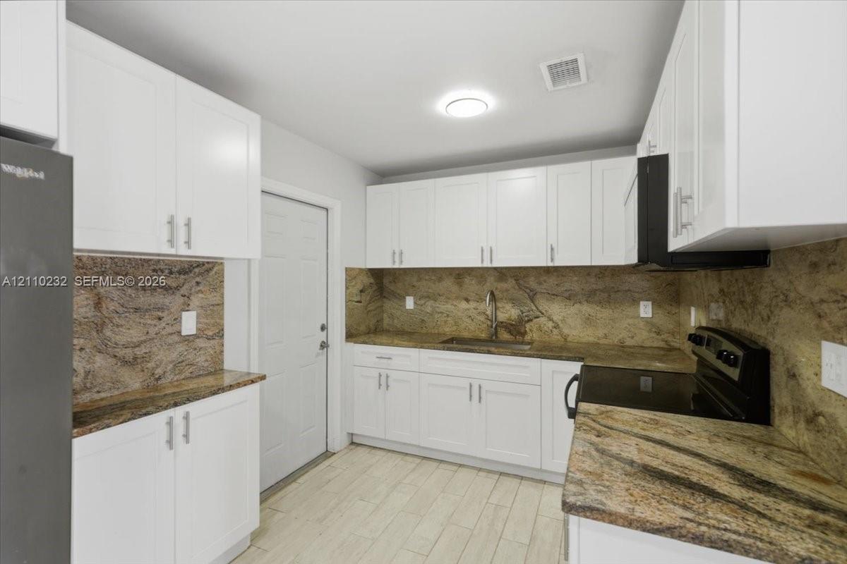 Kitchen featuring white shaker-style cabinetry, stone countertops with matching backsplash, wood-finish flooring, and black built-in appliances