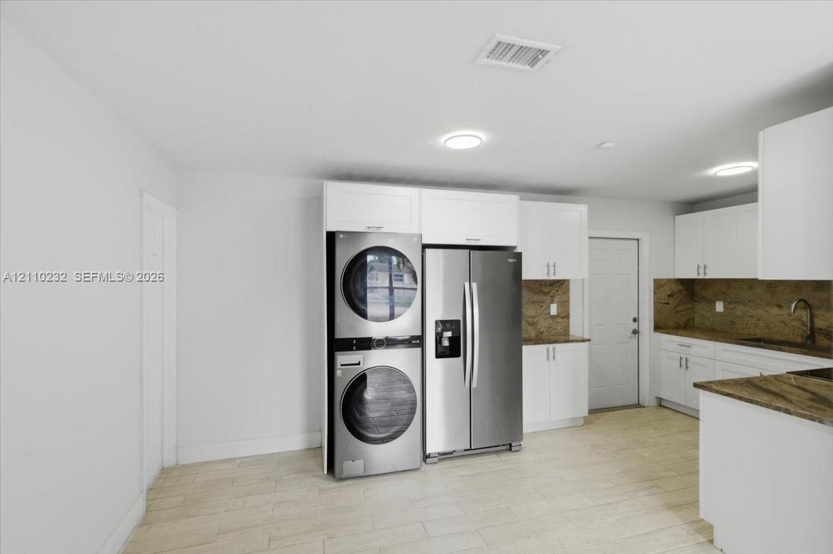 White cabinetry featuring shaker-style doors, stone-finish countertops, stainless steel appliances, and wood-finish flooring