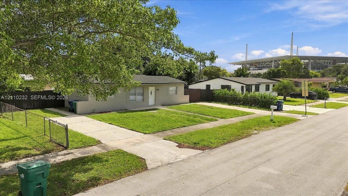 Single-story exterior featuring a concrete driveway, metal chain-link fencing, and a grass lawn