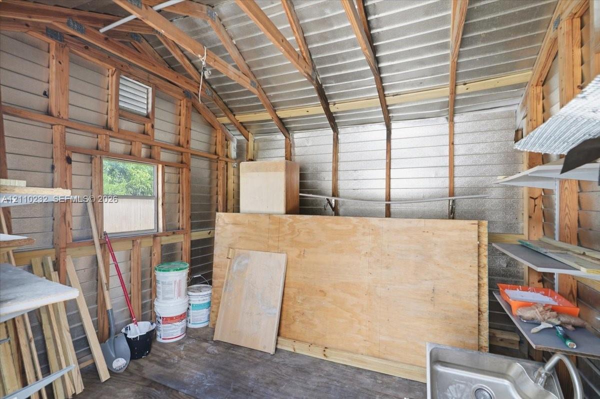 Outbuilding interior featuring exposed wood framing, metallic insulation, a utility sink, and fixed shelving