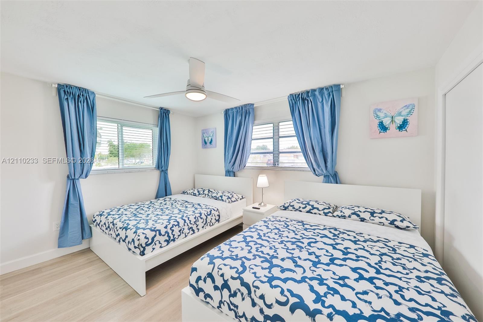 Bedroom featuring wood-finish flooring, dual horizontal sliding windows, and a central ceiling fan with integrated lighting