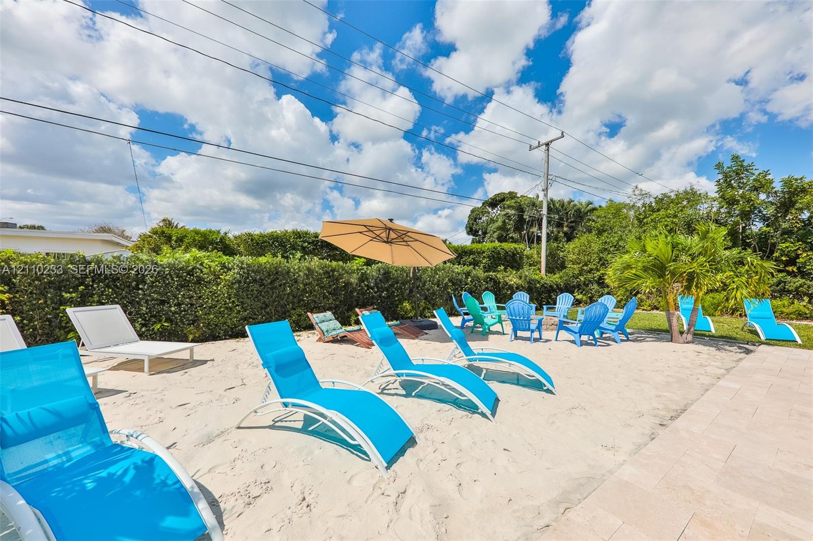 Outdoor space featuring a sand-covered ground, paver patio, and natural hedge perimeter