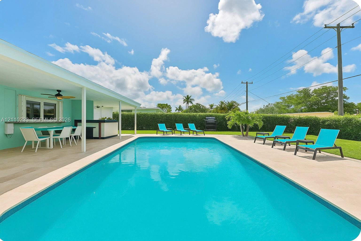 In-ground swimming pool with a surrounding paved deck, covered patio, and manicured hedge perimeter