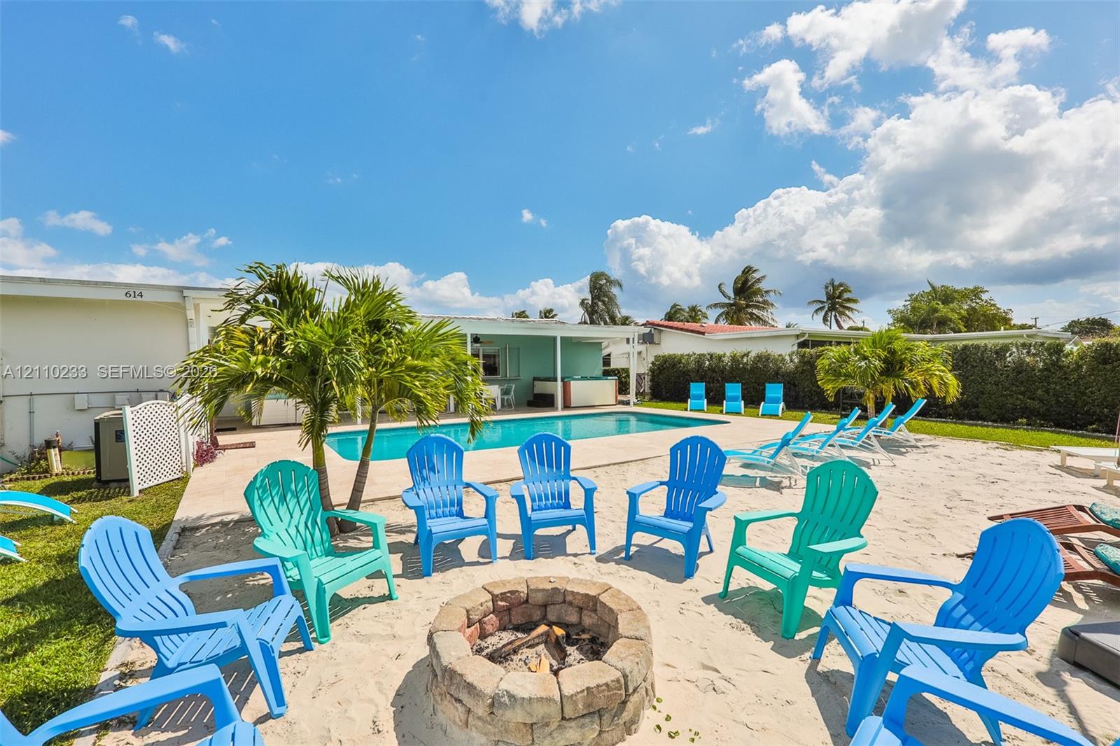 Rectangular swimming pool with a concrete surround, circular stone-block fire pit, and mature palm trees