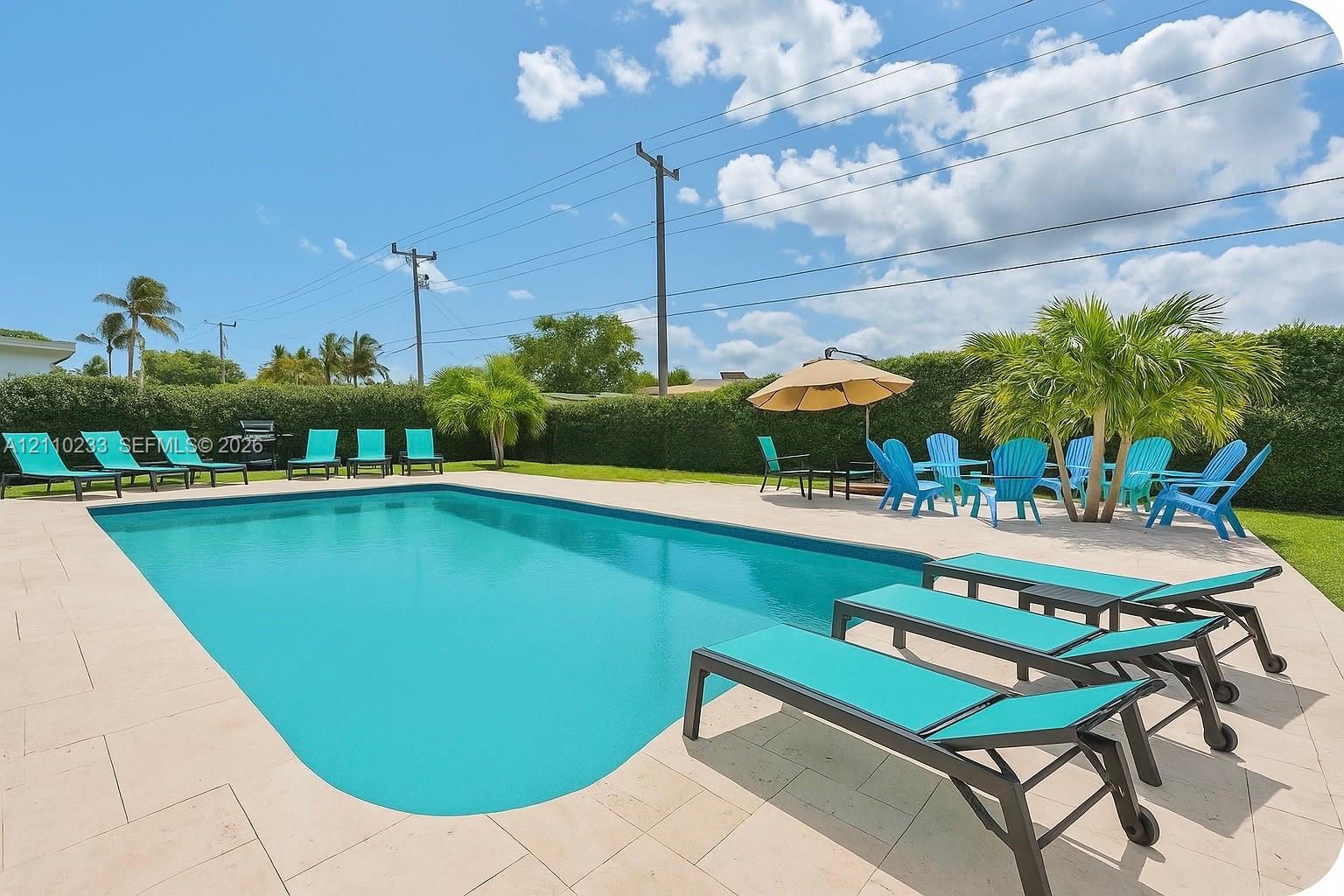 In-ground swimming pool featuring a light-toned stone paver deck and perimeter privacy hedging