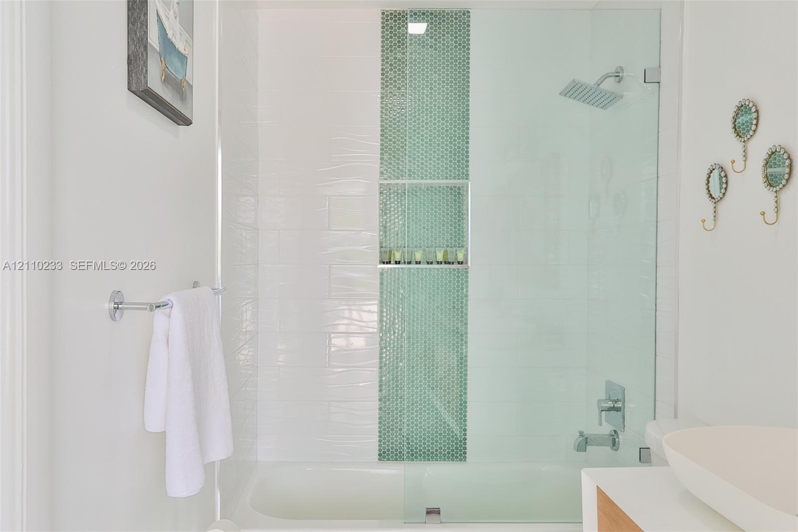 Shower and tub combination featuring white wall tiling, a vertical mosaic accent stripe, built-in recessed shelving, a glass shower panel, and a rectangular rainfall showerhead