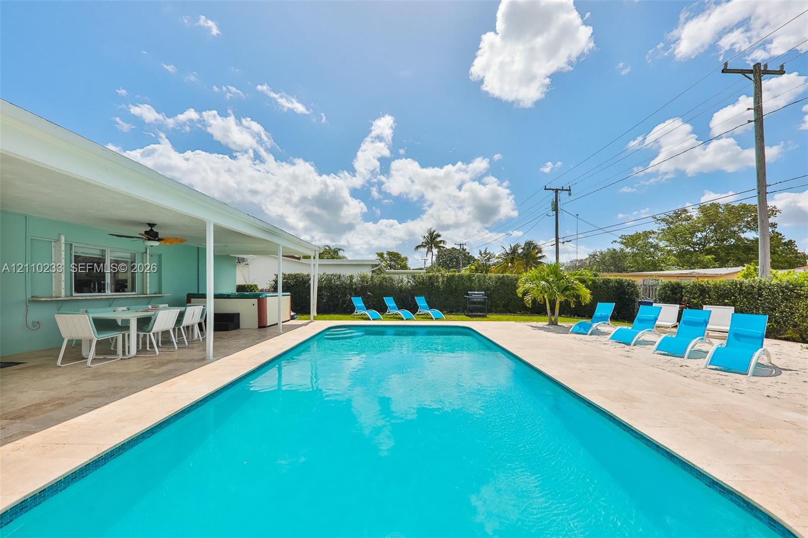 In-ground swimming pool featuring a concrete paver deck, covered outdoor patio, and perimeter hedge landscaping