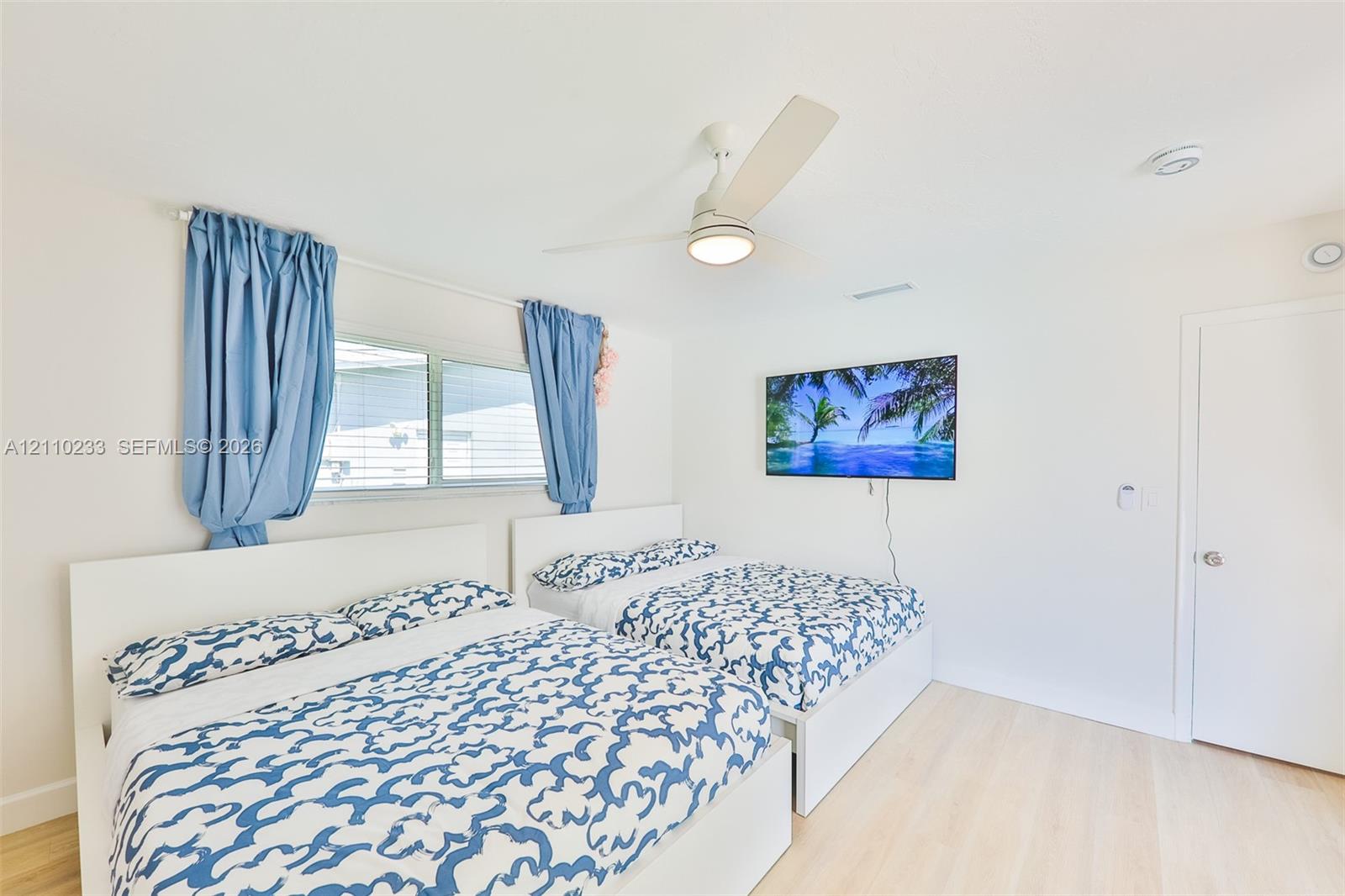 Neutral-toned room featuring wood-finish flooring, a white three-blade ceiling fan with integrated lighting, and a horizontal sliding window