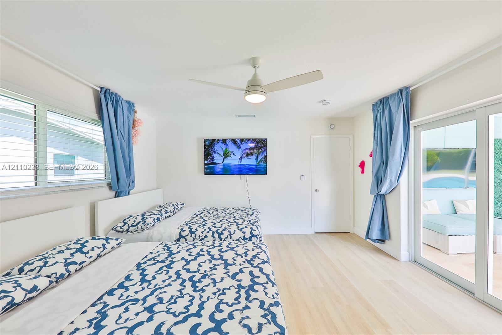 Light-toned wood-finish flooring, ceiling fan with integrated lighting, and glass sliding doors providing exterior exposure