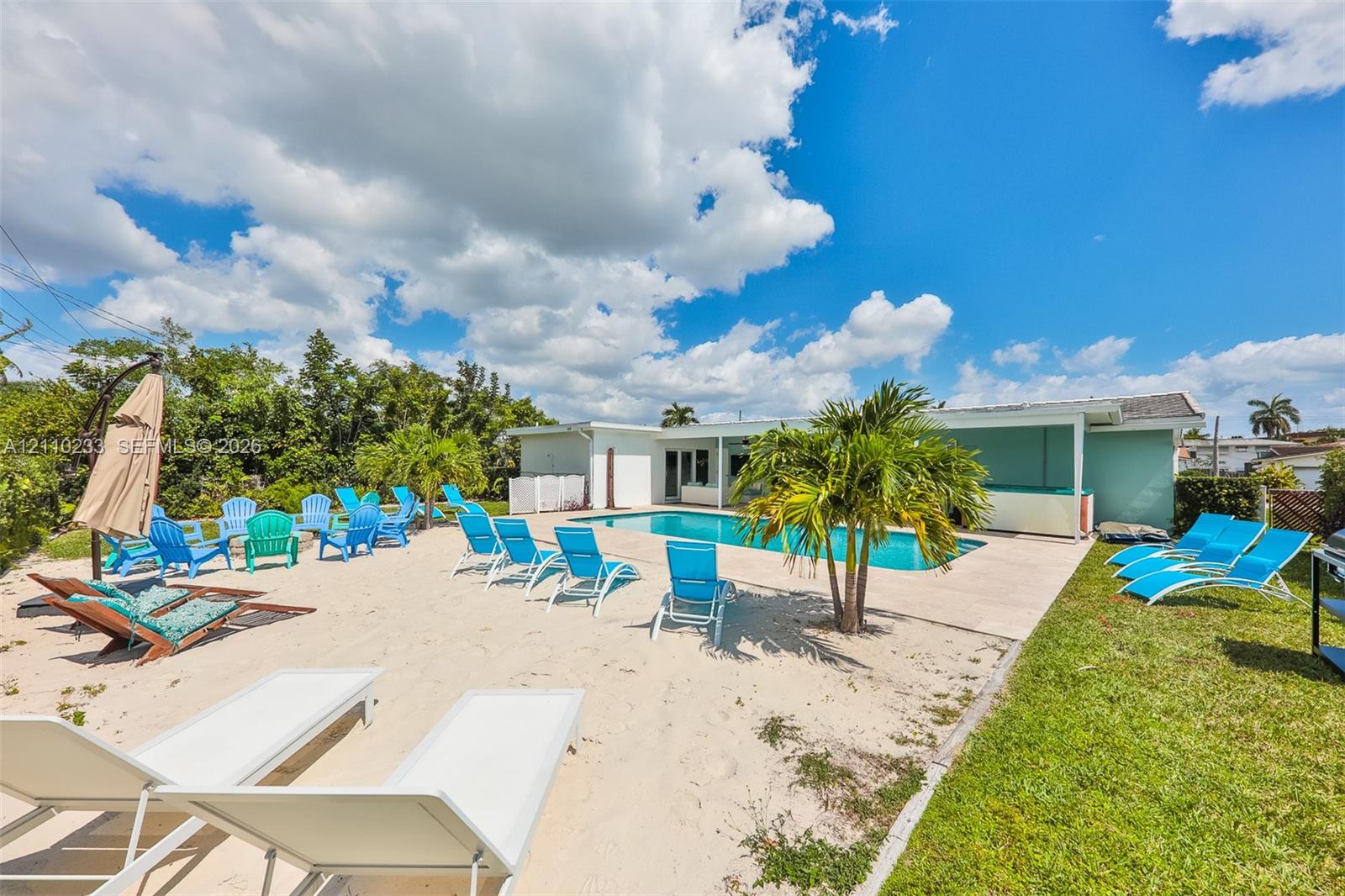 In-ground swimming pool with concrete decking, sand-surfaced patio area, and manicured lawn