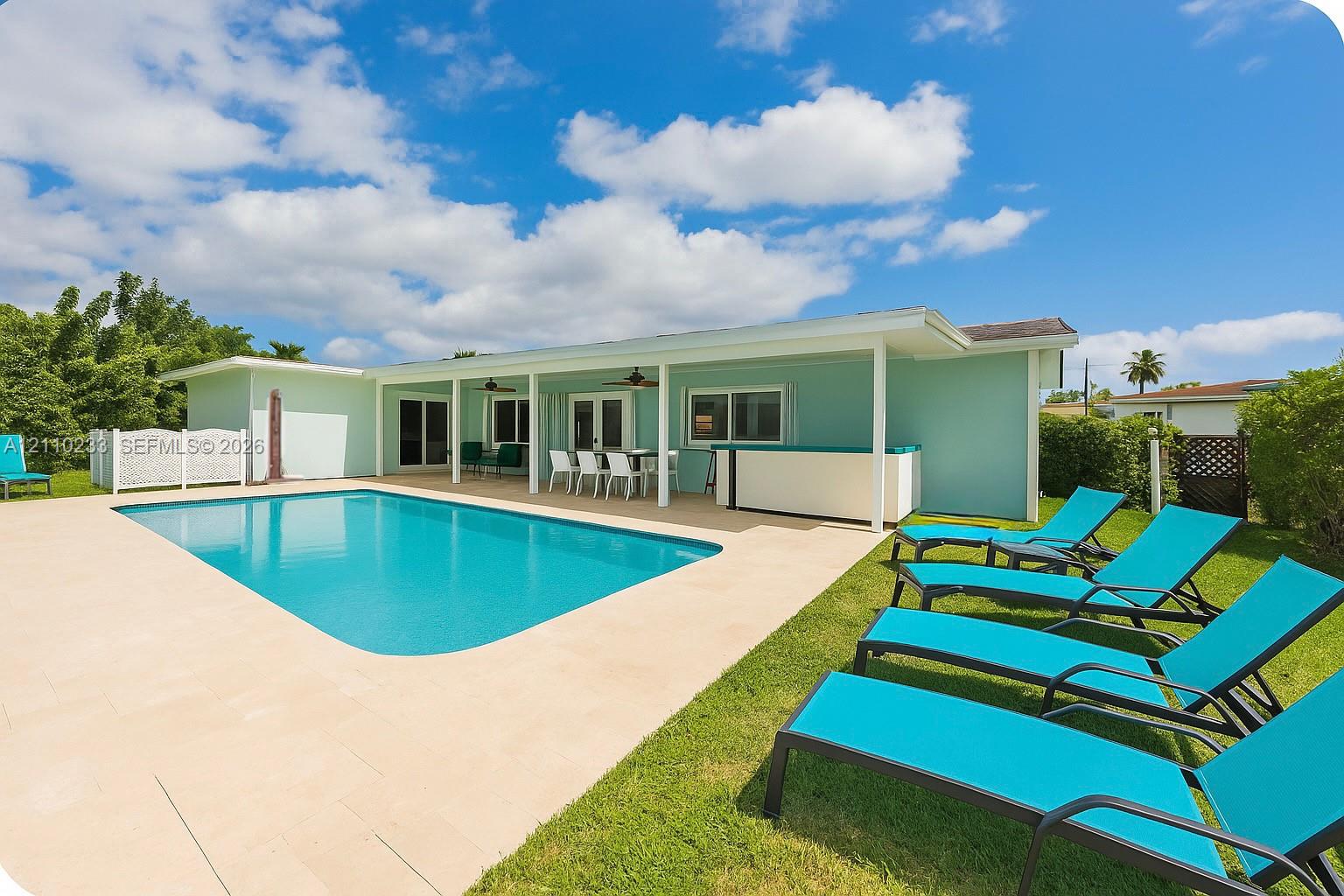 In-ground swimming pool featuring a concrete pool deck, covered patio, and built-in exterior bar