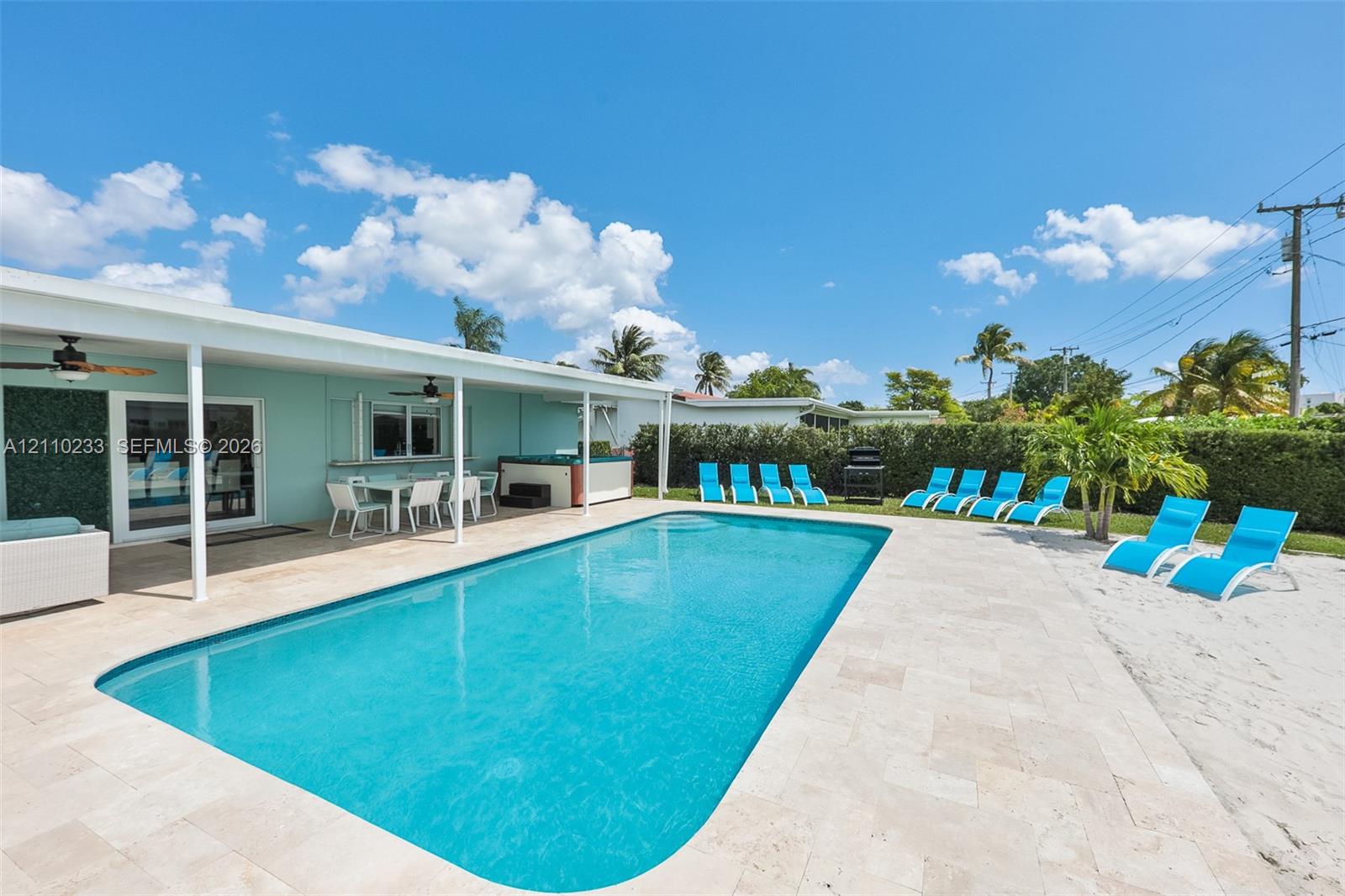 Outdoor area featuring an in-ground swimming pool, expansive stone paver pool deck, covered patio, integrated hot tub, and privacy hedge