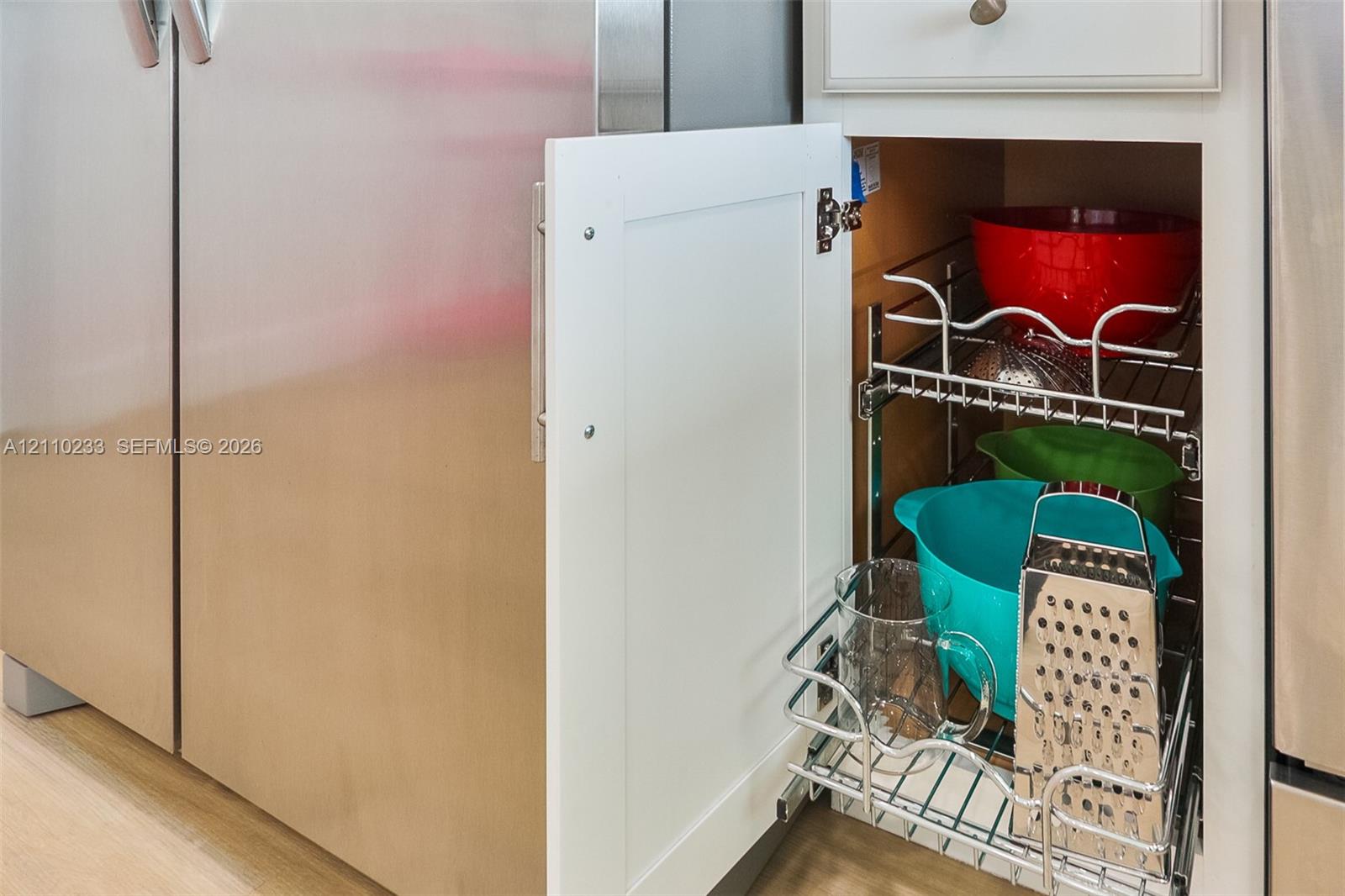 Custom white shaker-style cabinetry featuring an integrated pull-out chrome wire storage rack, set beside a stainless steel refrigerator