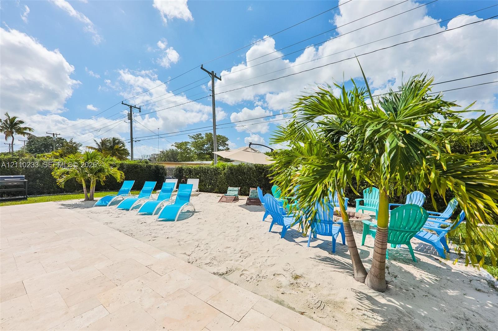 Outdoor living area featuring a light-toned stone paved patio, integrated sand-filled recreational space, and mature palm trees