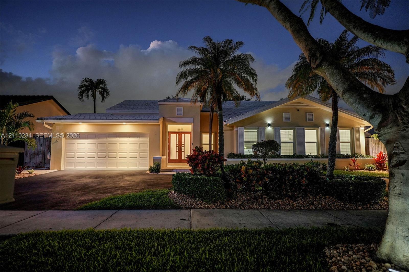 Single-story residence featuring a multi-paneled garage door, dual-entry front door with glass inserts, neutral exterior finish, pitched roofline, and landscaped front garden with mature palm trees
