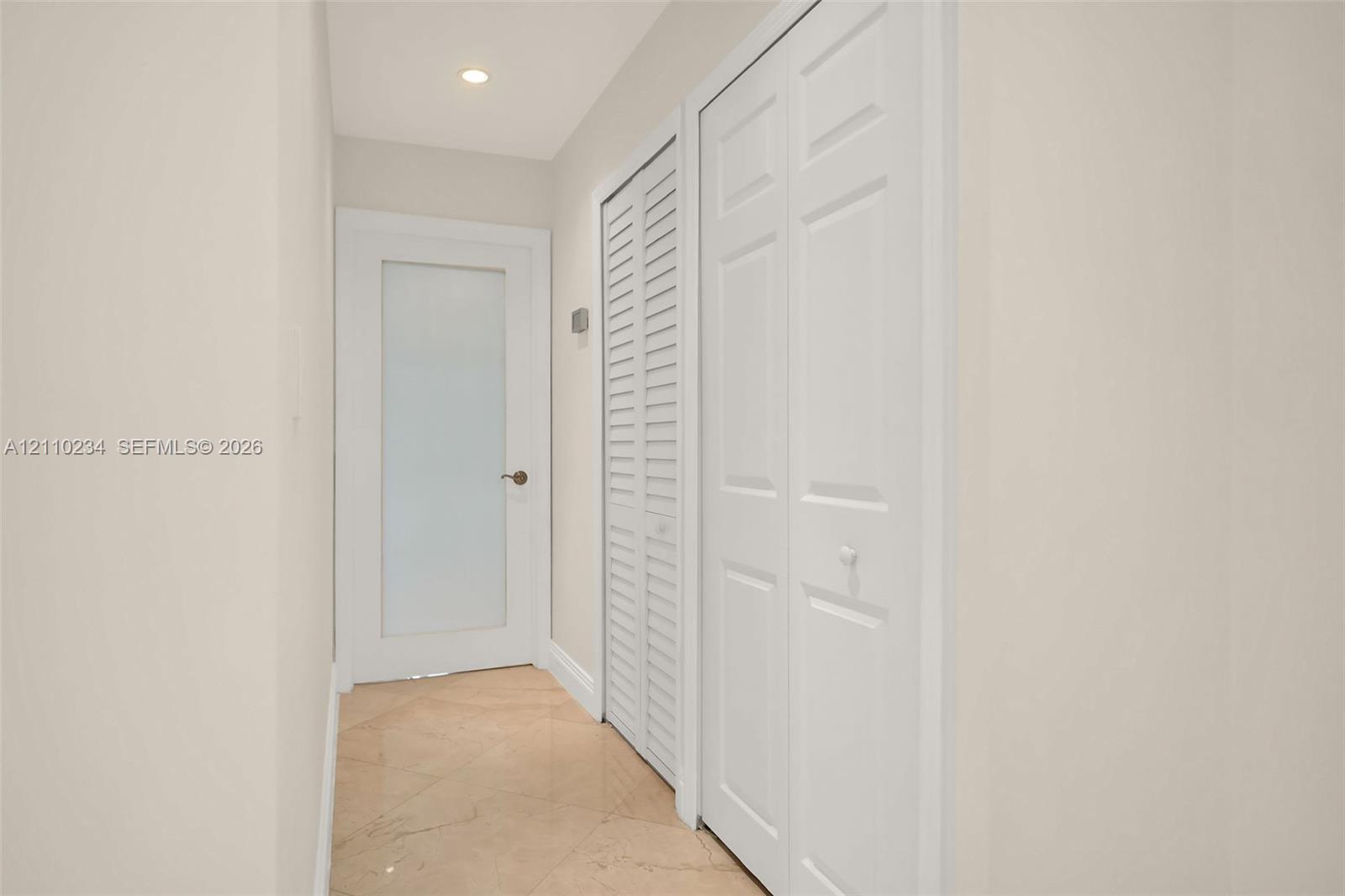 Neutral-toned interior space featuring stone flooring, a door with a frosted glass panel, and dual built-in closets with white louvered and paneled doors
