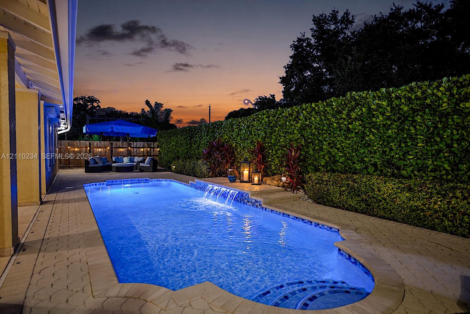 Backyard swimming pool featuring integrated water features, a paver stone deck, and mature privacy hedging