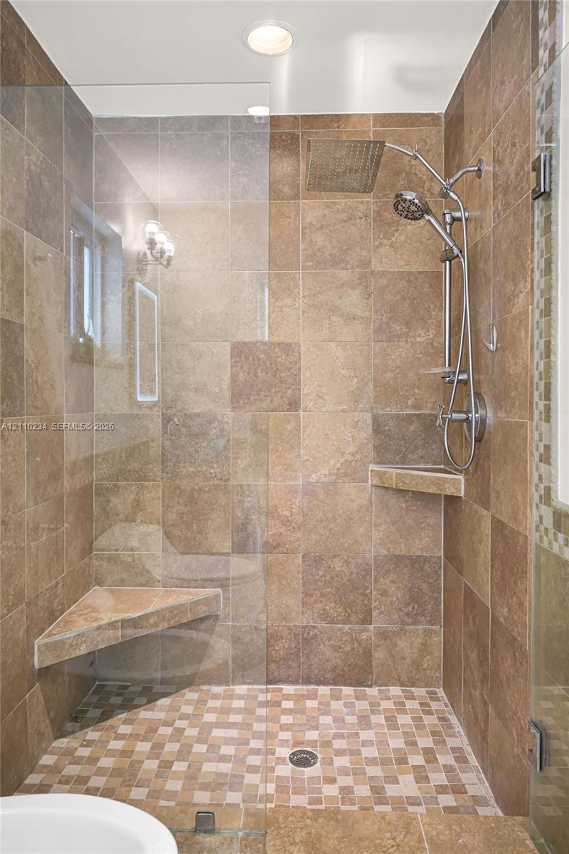 Walk-in shower featuring floor-to-ceiling stone-finish tile, a glass enclosure, dual shower