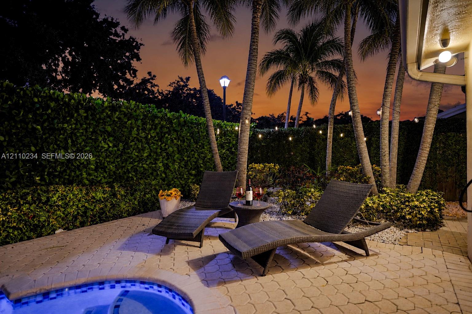 Paver patio featuring a built-in spa, mature palm trees, and privacy-focused hedge landscaping