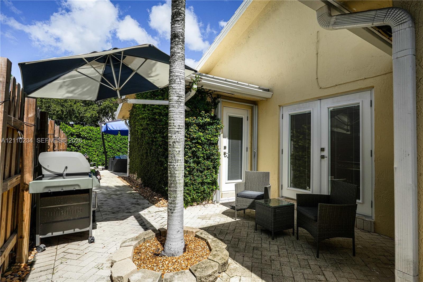 Outdoor patio featuring herringbone-patterned pavers, a circular stone-lined tree planter, and dual-pane glass entry doors