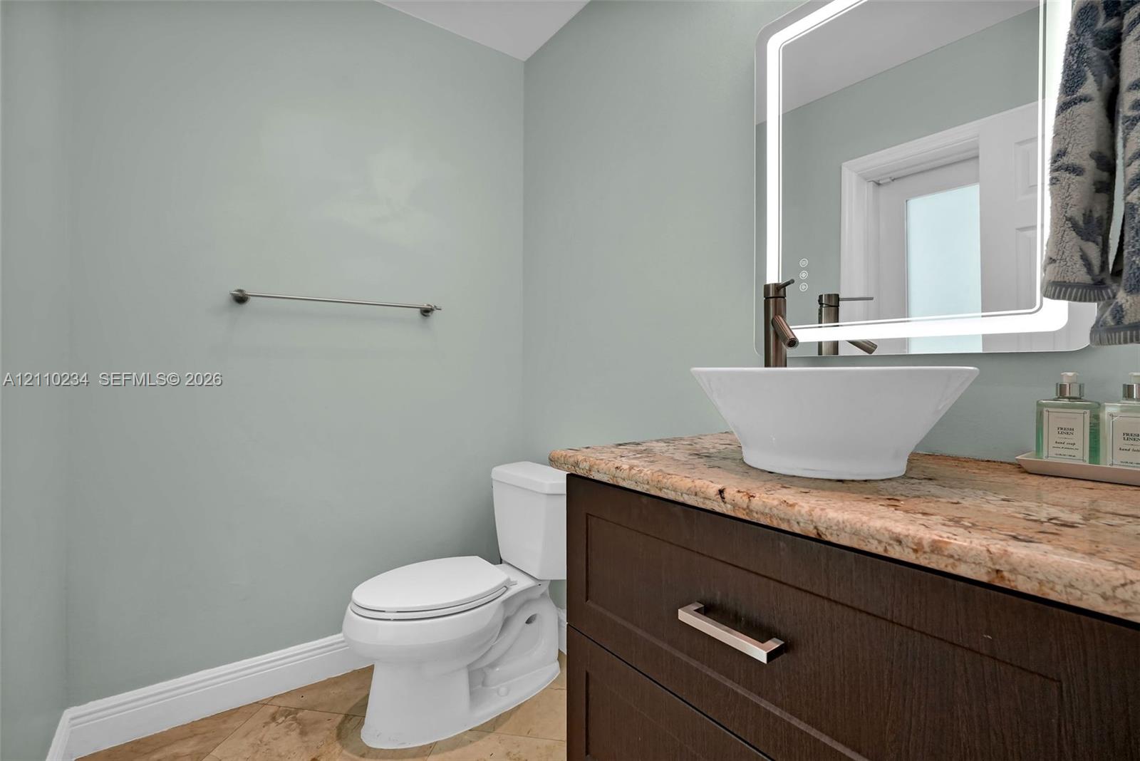 Dark wood vanity featuring a stone countertop, white vessel sink, brushed metal faucet, and an integrated LED-backlit mirror