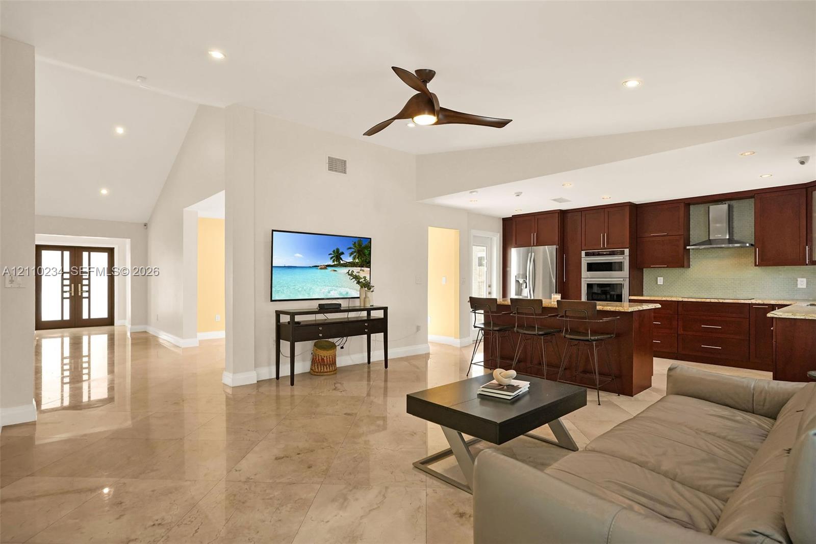 Open-concept living space featuring vaulted ceilings, polished stone tile flooring, recessed lighting, and a modern ceiling fan