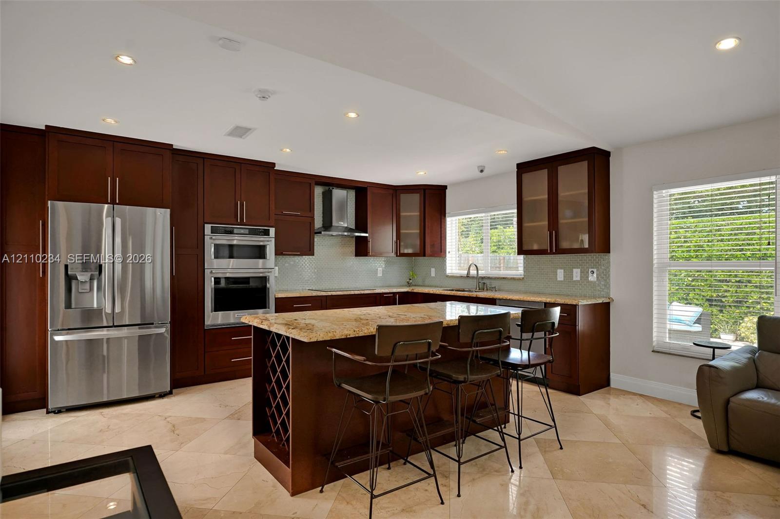 Kitchen featuring dark wood cabinetry, stainless steel appliances, stone countertops, integrated wine storage, and stone-finish flooring