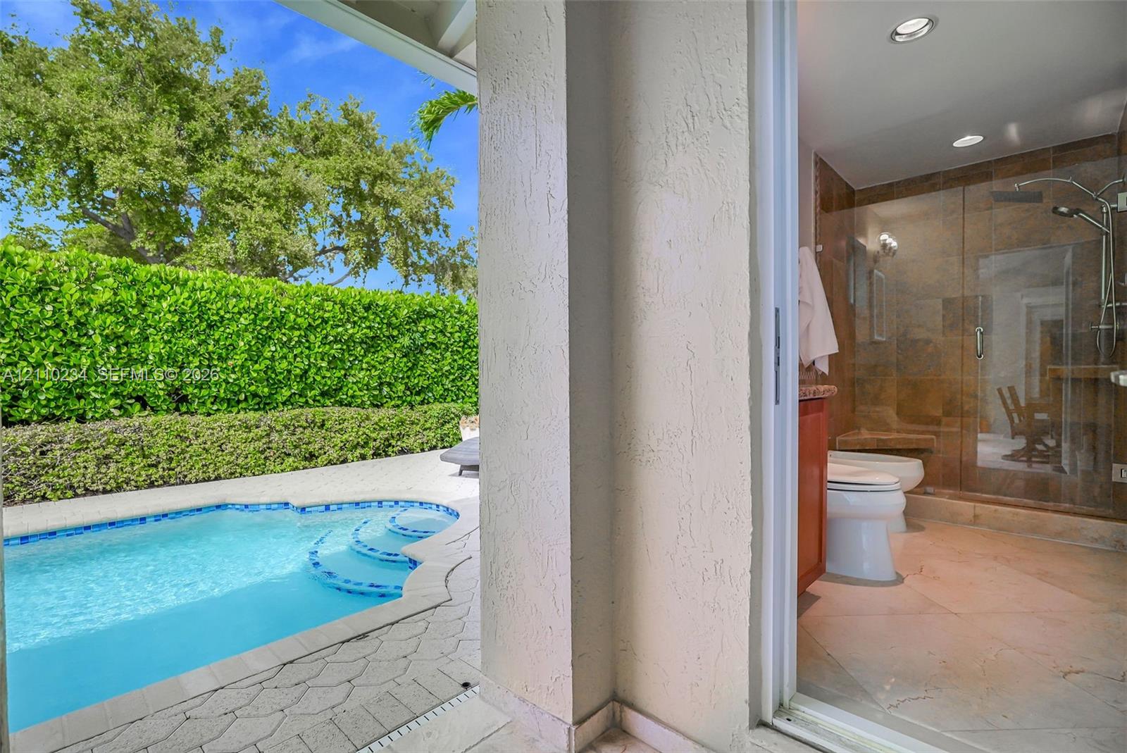 In-ground pool with stone paver surround, recessed shower lighting, glass-enclosed shower stall with tile wall, and stucco exterior walls