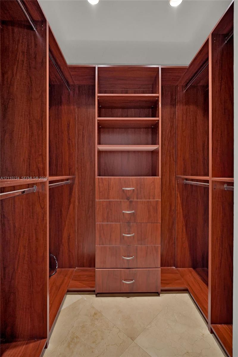 Custom walk-in closet featuring floor-to-ceiling wood-finish cabinetry, built-in shelving, a five-drawer dresser unit with metallic pulls, multiple integrated clothing rods, and tile flooring