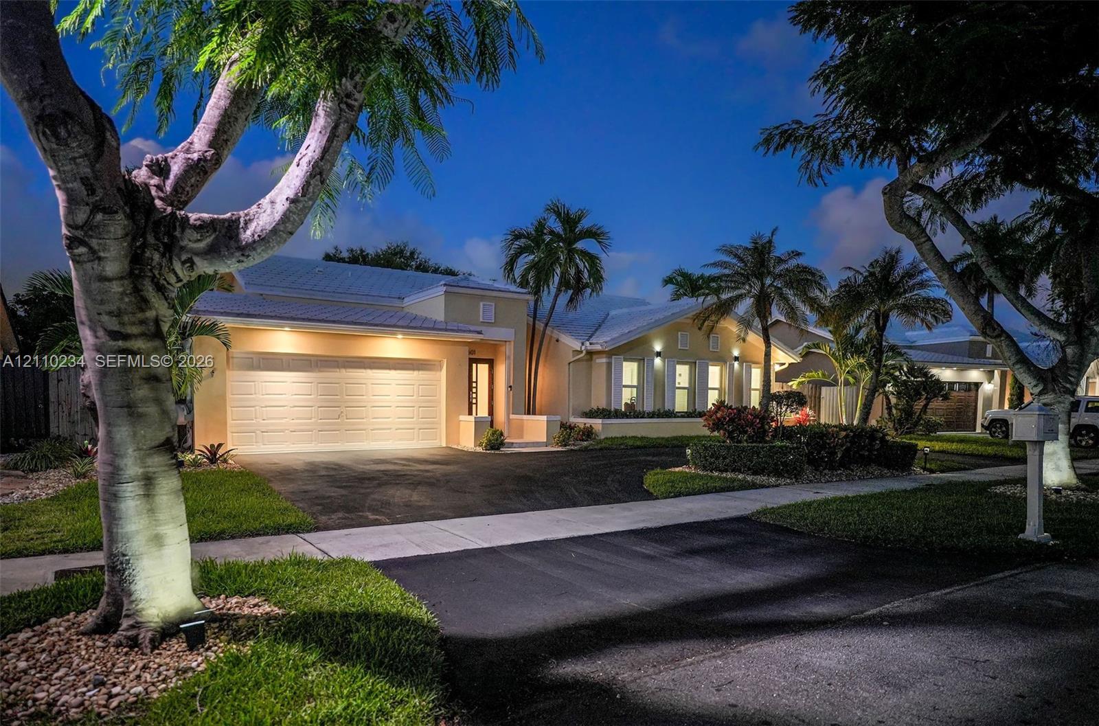 Single-story residence featuring a multi-car garage, metal roofing, expansive driveway, and integrated landscape lighting